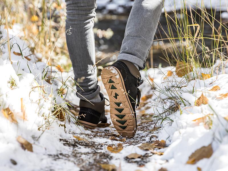 The image shows a man walking on a snowy trail, wearing the Phil Mid Men's Waterproof Sneakerboots in Mocha.